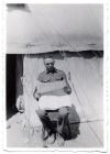 Photograph of a soldier reading a newspaper in front of a tent, at Idku, Egypt, 1930