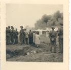 Photograph of soldiers and civilians observing the burning of the last remaining hut at Belsen Concentration Camp, taken in Germany, 21 May 1945