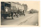 Photograph of soldiers of the 113 Light Anti-Aircraft Regiment, Royal Artillery (Territorial Army), in trucks and gun carriages, driving past a saluting base, taken in Germany, 8 May 1945