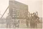 Photograph of soldiers standing in front of a sign stating that 