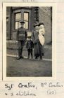 Photograph of a non-commissioned officer of the 6th Battalion The Durham Light Infantry with his wife and two children outside a house, captioned: Sgt. Coates, Mrs. Coates and 2 children, n.d. [1914 -