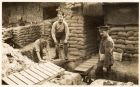 Photograph of a sergeant and two men of the 6th Battalion fitting duckboards outside a building reinforced with sandbags, [Ypres, Belgium], n.d. [1915]