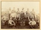 Photograph of a group of soldiers and a sergeant, possibly of the Royal Garrison Artillery, at camp, the winners of an unidentified trophy shield, n.d. [c.1908]